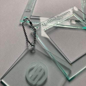 May include: Three clear acrylic quilting squares with a silver chain attached to one of the squares. The largest square has the text "Quilting Squares" etched into it. The smallest square has a monogram etched into it.
