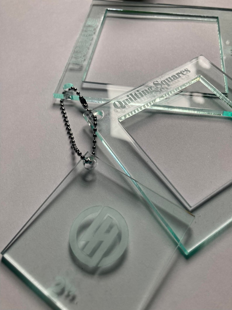 May include: Three clear acrylic quilting squares with a silver chain attached to one of the squares. The largest square has the text "Quilting Squares" etched into it. The smallest square has a monogram etched into it.