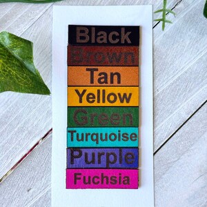 May include: A vertical stack of eight leather swatches, each with a different color and the color name printed in black. The colors are black, brown, tan, yellow, green, turquoise, purple, and fuchsia.