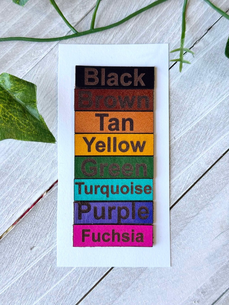 May include: A vertical stack of eight leather swatches, each with a different color and the color name printed in black. The colors are black, brown, tan, yellow, green, turquoise, purple, and fuchsia.