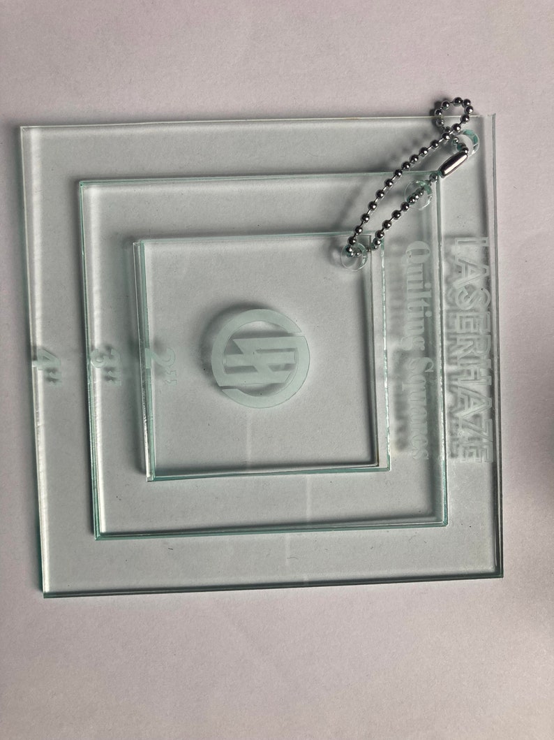 May include: Three clear glass squares with a chain attached to the largest square. The squares are labeled "Lagenfaze Quilting Squares".
