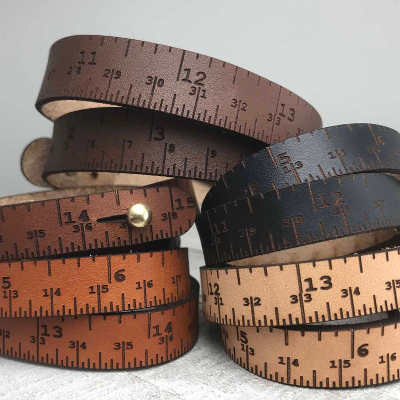 May include: Three leather bracelets with a ruler design. The bracelets are brown, black, and tan. The ruler markings are in inches and fractions of an inch.