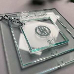 May include: Set of three clear glass quilting squares with a keychain. The squares are 2 inches, 3 inches, and 4 inches. The squares have a logo with the letters "WH" inside a circle.
