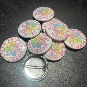 May include: A set of eight colorful button pins with a flower design and the text "Don't Worry Be Happy".