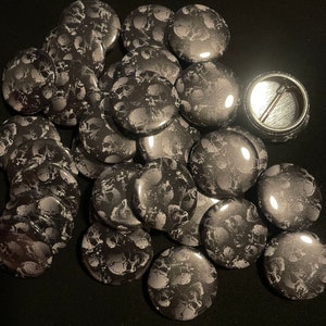 May include: A collection of 1.25 inch button pins featuring a black and white skull pattern. The buttons are round and have a shiny finish.