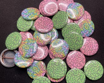 Puede incluir: Una colección de 25 botones redondos con un diseño de cerebro. Los botones están disponibles en tres variaciones de color: rosa, verde y un remolino multicolor.