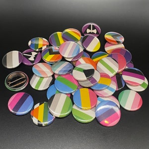 May include: A collection of colorful round pins with various designs, including stripes, geometric shapes, and abstract patterns. The pins are made of metal and have a shiny finish.
