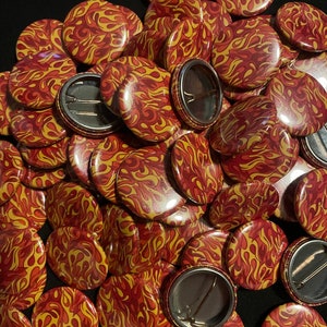 May include: A large pile of round, red and yellow buttons with a flame pattern. The buttons have a silver metal back with a pin.