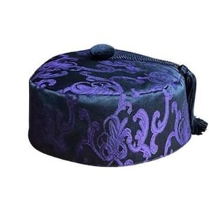 May include: A black and purple patterned hat with a tassel. The hat has a round shape and a flat top.