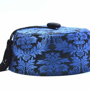 Op de afbeelding: Een blauw en zwart patroon fez hoed met een zwarte kwast en een kleine zwarte knop bovenop. De hoed heeft een bloemenmotief en staat tegen een witte achtergrond.