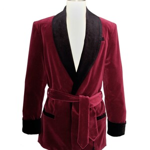 May include: A burgundy velvet robe with a black satin shawl collar and a matching black satin sash. The robe has long sleeves and a tie closure at the waist.
