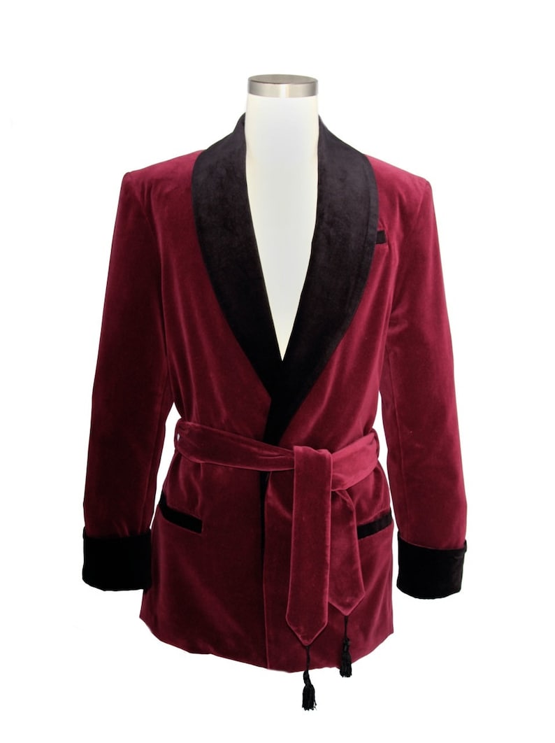 May include: A burgundy velvet robe with a black satin shawl collar and a matching black satin sash. The robe has long sleeves and a tie closure at the waist.