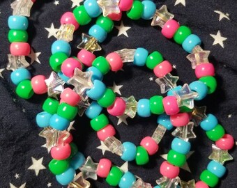 May include: A set of four colorful beaded bracelets with star-shaped charms. The bracelets are made with pink, green, and blue beads.