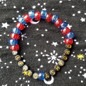 May include: A black beaded bracelet with gold letters spelling "ALFRED ASHFORD" and red and blue spacer beads.