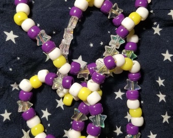 May include: A purple and yellow beaded bracelet with iridescent star-shaped beads. The bracelet is made of small, round beads and is tied together in a knot.
