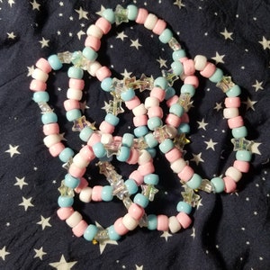 May include: A set of three colorful beaded bracelets with star-shaped charms. The bracelets are made with pink, blue, and white beads.