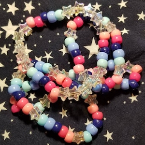 May include: A multi-colored beaded bracelet with star-shaped beads. The bracelet is made with pink, blue, and light blue beads.