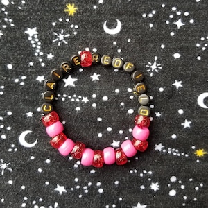 May include: A pink and red beaded bracelet with the name "CLAIRE REDFIELD" spelled out in black beads.