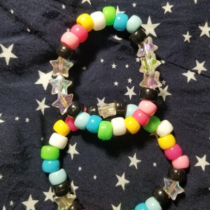 May include: Two colorful beaded bracelets with star-shaped charms. The bracelets are made with rainbow-colored beads and black spacer beads. The star charms are clear with iridescent accents.