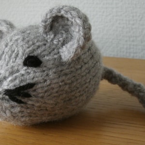 May include: A handmade gray knitted mouse toy with black eyes and whiskers, and a pink nose. The mouse has a long tail and is made of soft yarn. A cute and cuddly toy for children.