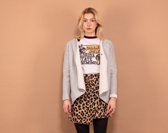Puede incluir: Una mujer lleva una chaqueta de punto gris sobre una camiseta blanca con el texto "Orange Bowl Florida State Seminoles" impreso en ella. Lleva una falda de estampado de leopardo y medias negras con botines negros.