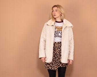 Puede incluir: Una mujer con una chaqueta de piel sintética blanca con una falda de estampado de leopardo y medias negras. Lleva botines negros de tobillo. La chaqueta tiene un cuello grande y la falda es una minifalda.