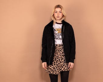Puede incluir: Una mujer con una chaqueta bomber negra con cuello de piel, una camiseta blanca con el texto "Dance So Hard" y una falda de estampado de leopardo. Lleva medias negras y botas negras de combate.