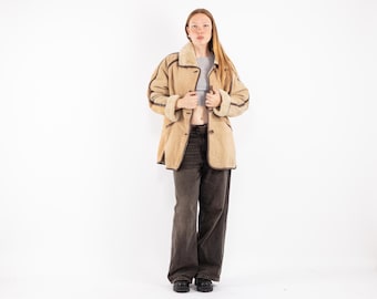 Puede incluir: Una chaqueta de ante marrón con cuello de piel de oveja y ribetes marrones. La chaqueta la lleva puesta una persona con el pelo largo y rojo.
