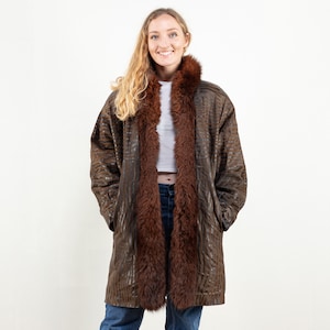 May include: A brown leather coat with a brown fur collar. The coat has a zipper closure and pockets. The model is wearing blue jeans.