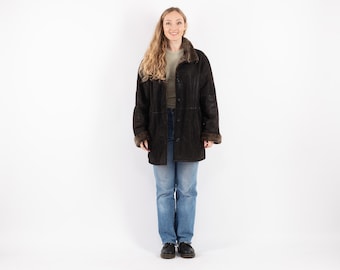 May include: A brown suede shearling coat with a fur collar and a button closure. The coat is worn by a person with long blonde hair and blue jeans.