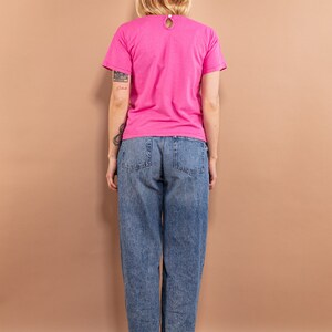 May include: A woman wearing a pink t-shirt and blue jeans. The t-shirt has a round neckline and short sleeves.