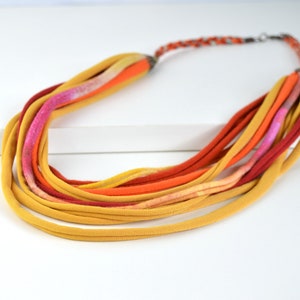 May include: A multi-strand necklace made of fabric in shades of yellow, orange, and red. The necklace is made of multiple strands of fabric that are tied together at the ends.