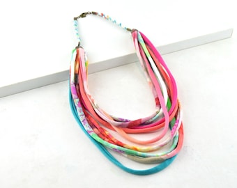 Op de afbeelding: Meerlaags ketting gemaakt van kleurrijke stofstroken. De ketting is gelaagd met verschillende kleuren en patronen, waaronder roze, oranje, groen en blauw.