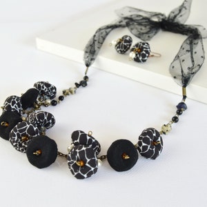 Puede incluir: Un collar con estampado en blanco y negro con bolas de tela negra y una cinta de tul negra. El collar se combina con pendientes a juego.