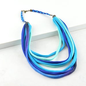 May include: A multi-strand necklace made of blue and turquoise fabric. The necklace is layered and has a braided fabric detail at the top.