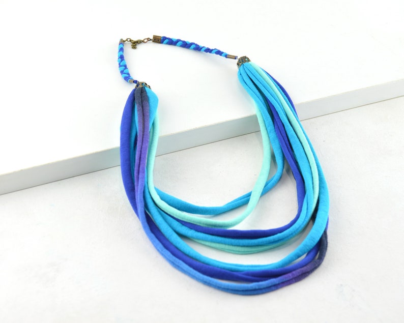 May include: A multi-strand necklace made of blue and turquoise fabric. The necklace is layered and has a braided fabric detail at the top.