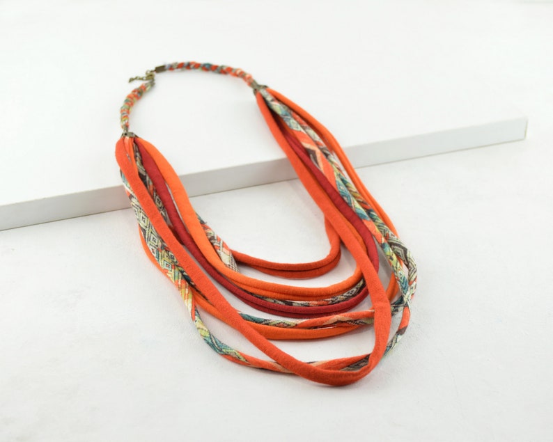 May include: A multi-strand necklace made of orange fabric with a paisley pattern. The necklace is layered and has a simple clasp.