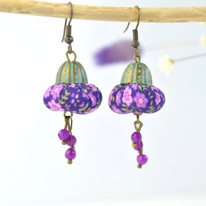 May include: Purple and pink floral fabric dangle earrings with a turquoise and gold top and purple beads hanging from the bottom.