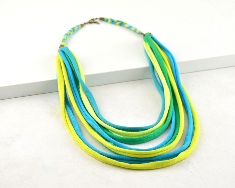 May include: A multi-strand necklace made of woven fabric in shades of green and blue.