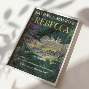 May include: A white framed book cover with a green and purple floral design. The title "REBECCA" is in gold lettering and the author is "DAPHNE du MAURIER". The text below reads "A brilliant novel of an unforgettable woman, by the author of JAMAICA INN."