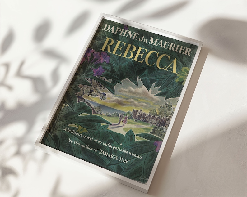 May include: A white framed book cover with a green and purple floral design. The title "REBECCA" is in gold lettering and the author is "DAPHNE du MAURIER". The text below reads "A brilliant novel of an unforgettable woman, by the author of JAMAICA INN."