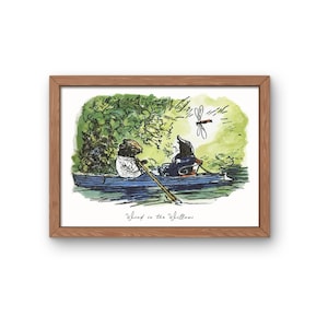 May include: A framed print featuring a watercolor illustration of two anthropomorphic animals in a rowboat. The artwork, titled "Wind in the Willows," depicts a serene scene with lush greenery and a dragonfly. The frame is made of wood.