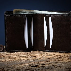 May include: A brown leather wallet with multiple card slots and a billfold. The wallet is open and a dollar bill is visible inside.
