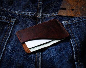 May include: A brown leather wallet with a white card and cash inside, sitting in a blue denim pocket.