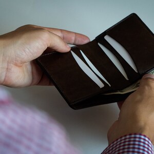 May include: A brown leather wallet with multiple card slots is being opened to reveal a dollar bill.