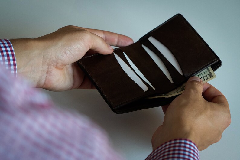 May include: A brown leather wallet with multiple card slots is being opened to reveal a dollar bill.