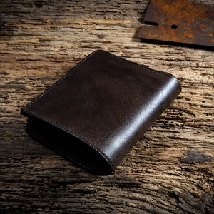 May include: A dark brown leather wallet on a rustic wooden surface.