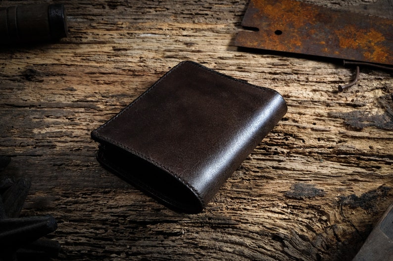 May include: A dark brown leather wallet on a rustic wooden surface.