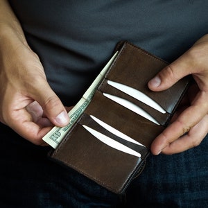 May include: A brown leather wallet with a zip fastening, open to show a dollar bill and several credit cards.