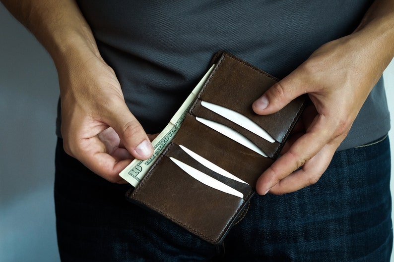 May include: A brown leather wallet with a zip fastening, open to show a dollar bill and several credit cards.
